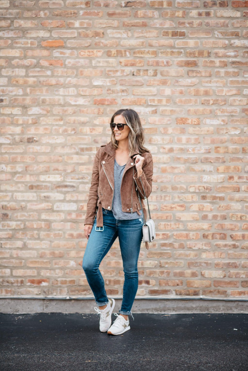 Grey tee, moto jacket, denim, sneakers, sunglasses, crossbody bag