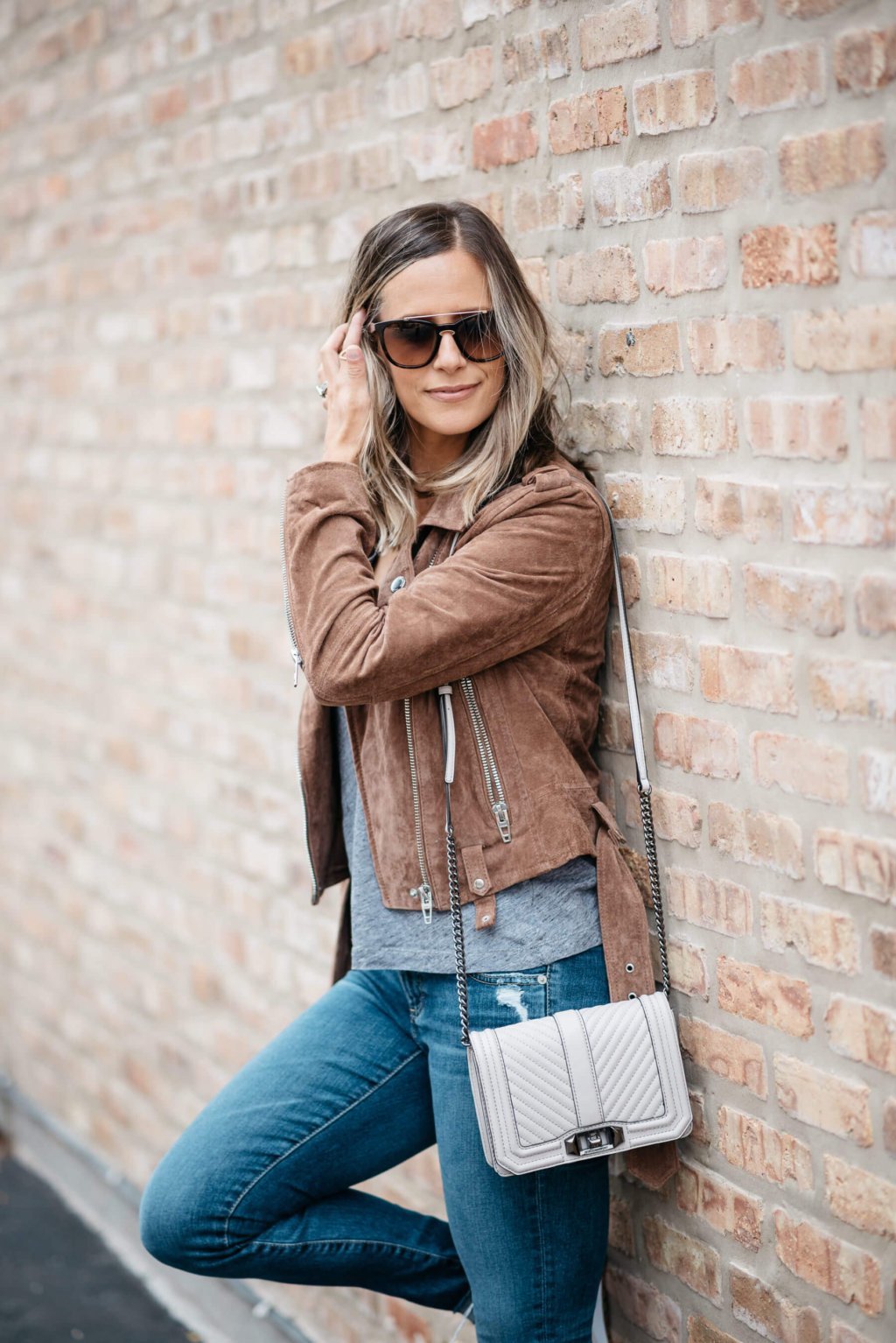 Grey tee, moto jacket, denim, sneakers, sunglasses, crossbody bag