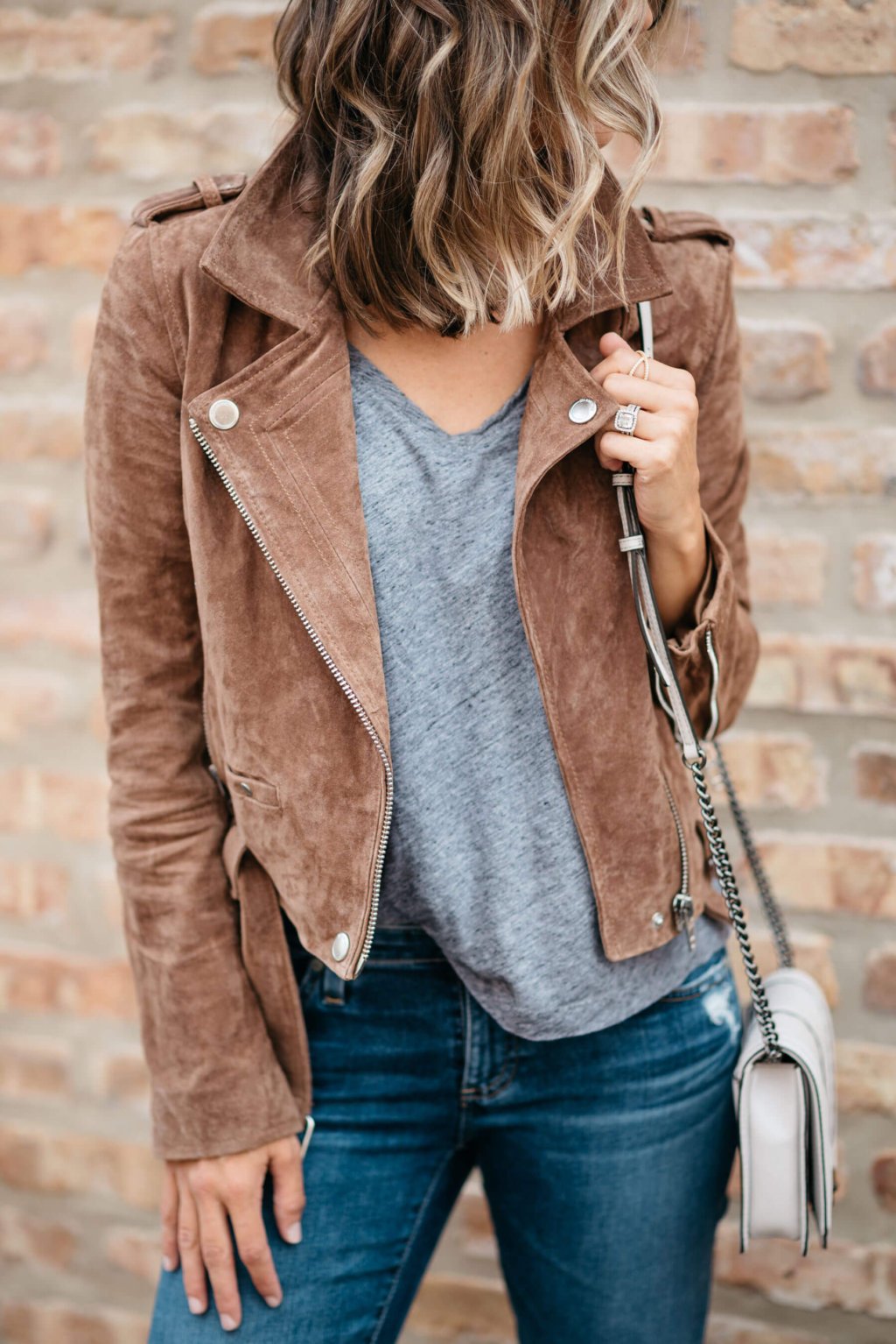 Grey tee, moto jacket, denim, sneakers, sunglasses, crossbody bag