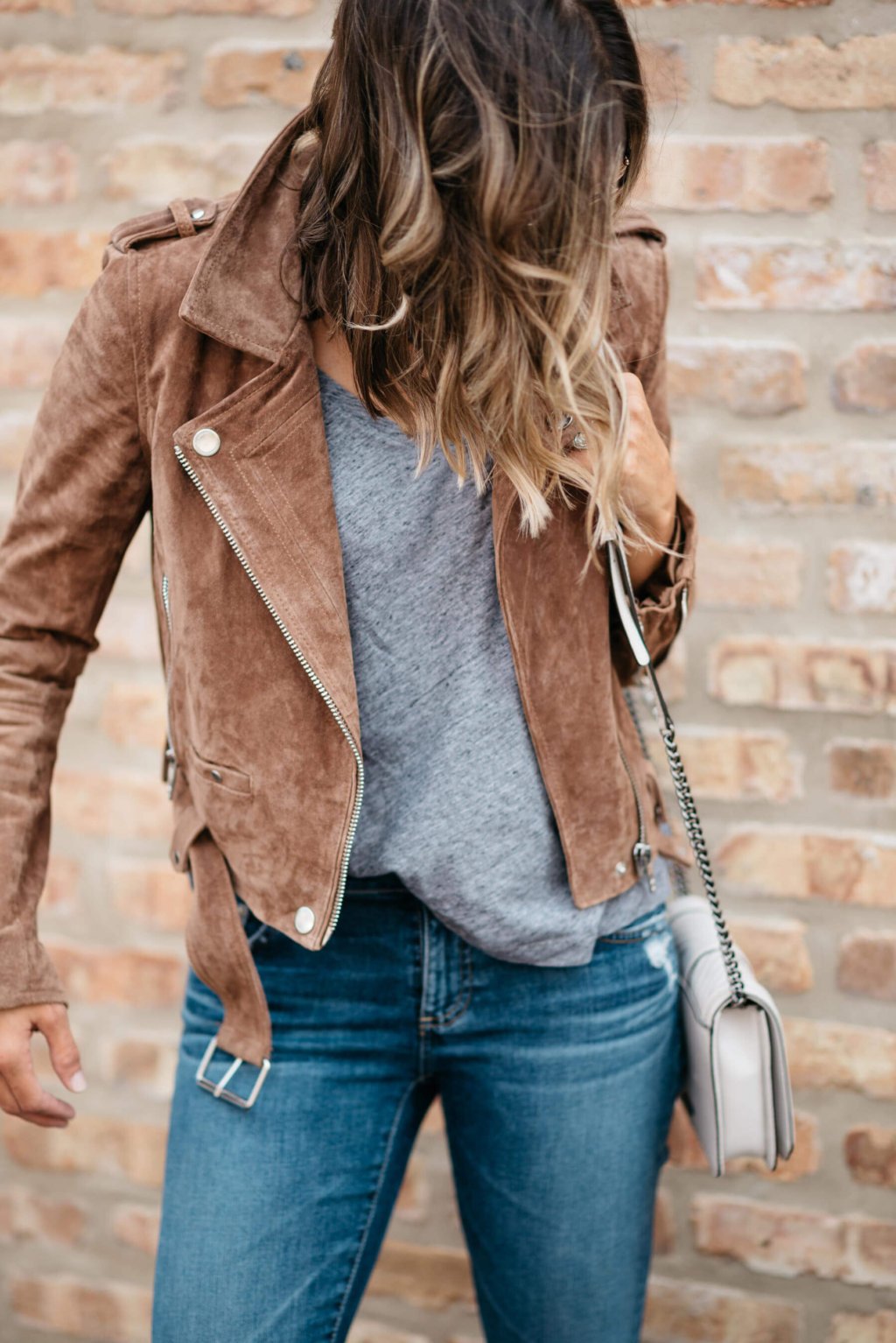 Grey tee, moto jacket, denim, sneakers, sunglasses, crossbody bag