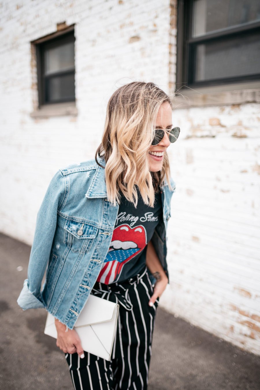 Band tee, striped pants, denim jacket, heels, clutch, sunglasses